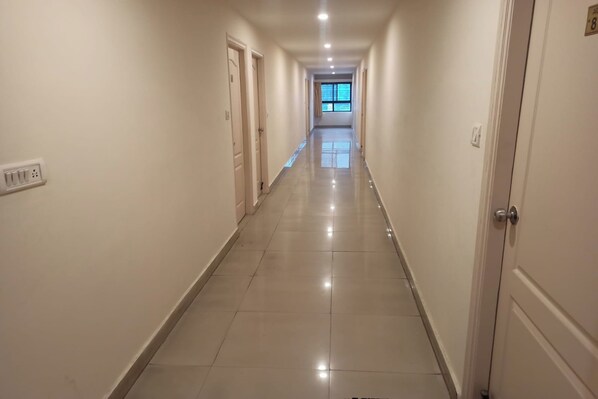 A long, narrow hotel corridor with doors on both sides, a tiled floor, and a window at the end. - Hotel Rainbow (Bengaluru)