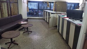 A small, compact hotel room with a sofa, two small tables, a kitchenette, and a large window offering a view of the street. - Hotel Rainbow (Bengaluru)