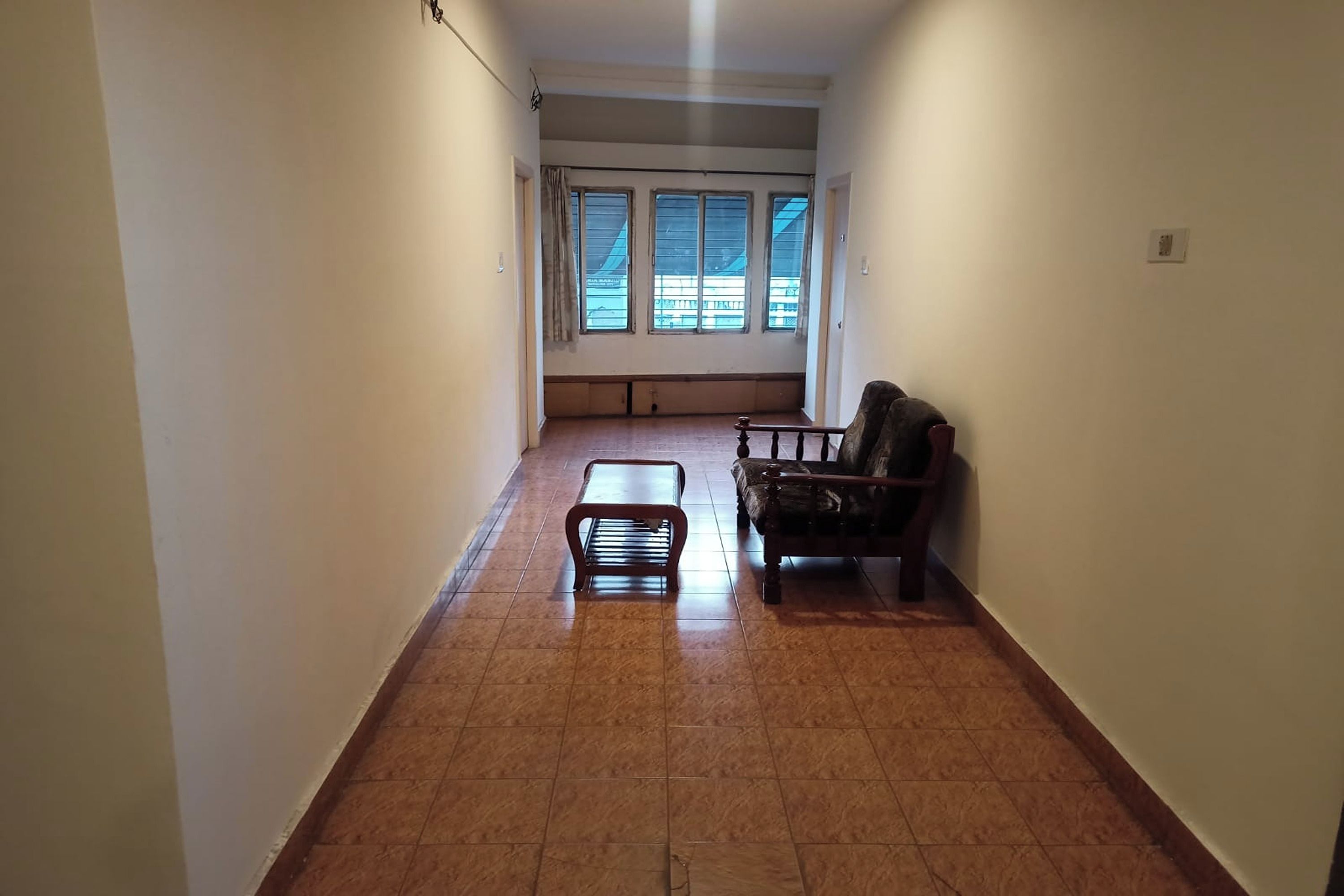 A narrow hallway with a wooden bench and a sofa, leading to a window with blinds.