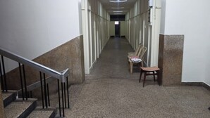 A long, narrow hallway with a staircase on the left and chairs on the right. - Hotel Rainbow (Bengaluru)