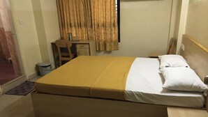 A single bed with a wooden headboard, a bedside table, a small desk, and a chair. - Hotel Rainbow (Bengaluru)