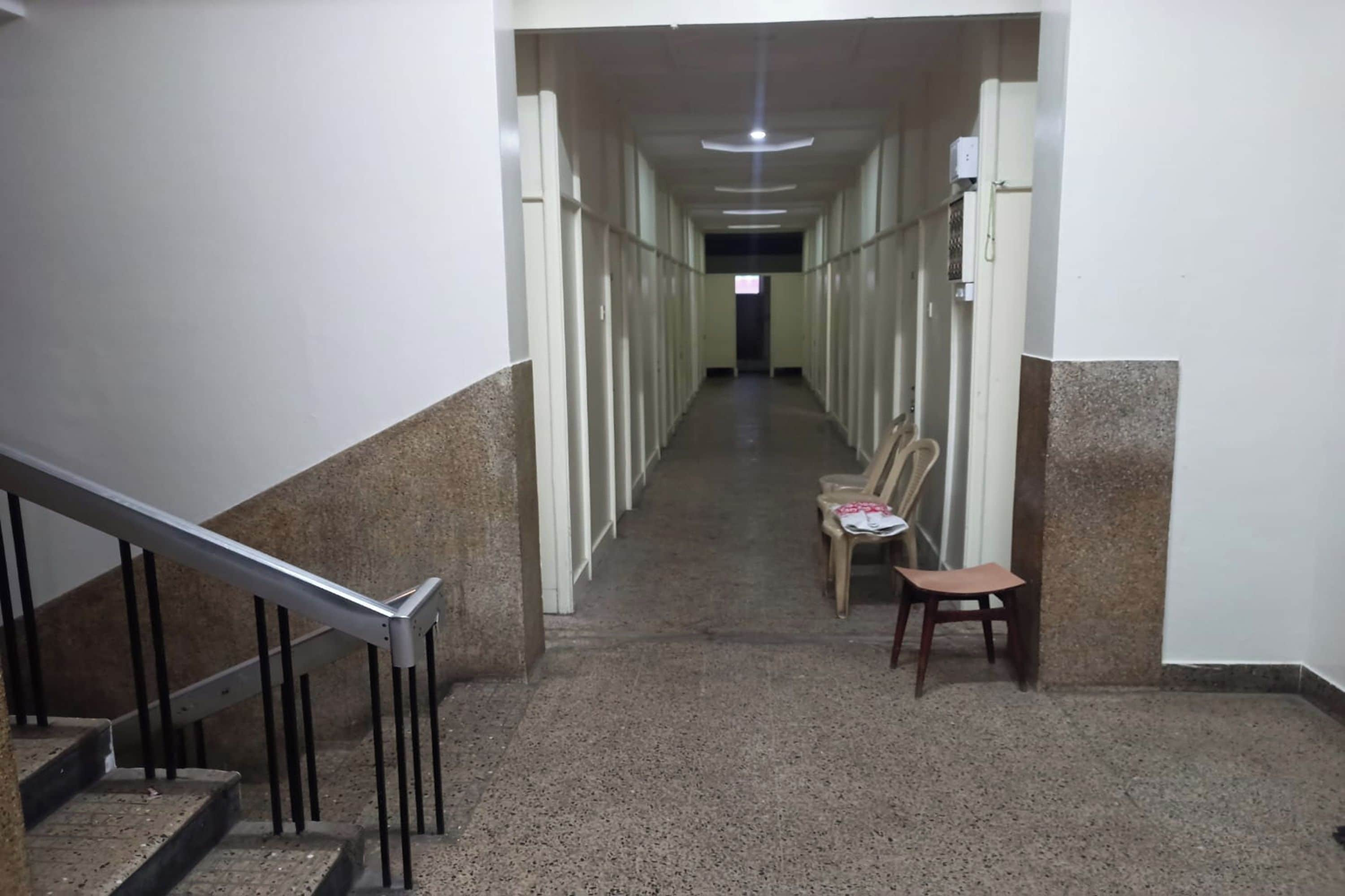 Un long couloir étroit, avec un escalier sur la gauche et des chaises sur la droite.