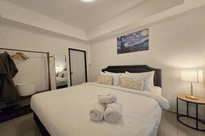 A neatly made bed with rolled towels, a bedside lamp, a painting on the wall, and a mirror with a wooden hanger. - Breezy Bliss Home (Chiang Mai)