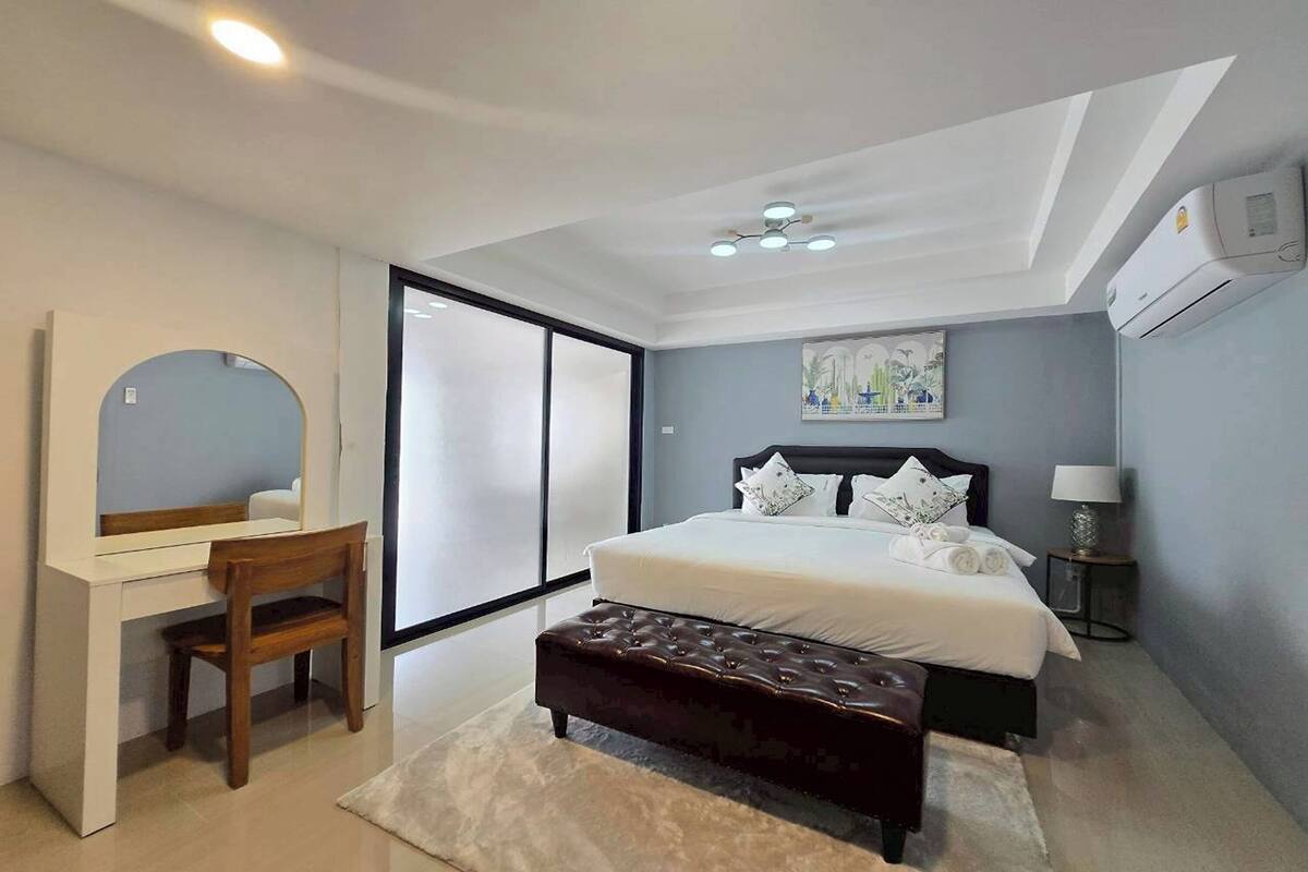 A bedroom with a bed, a desk, a chair, a bench, a mirror, and a painting on the wall.