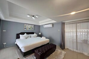 A modern bedroom with a large bed, a dark-toned bench, an air conditioning unit, and a ceiling light fixture. - Breezy Bliss Home (Chiang Mai)