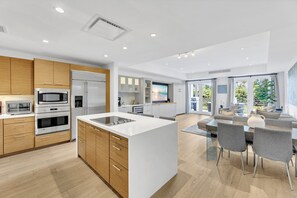 A modern kitchen with built-in appliances, a central island, and a dining area with grey chairs. - Modern Luxury in Tropical Paradise at Bahia Beach Resort within the Four Seasons (Río Grande)