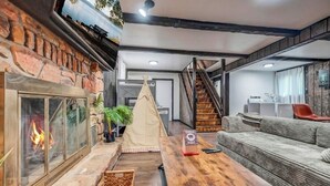 Un salon chaleureux avec une cheminée, une table en bois, un canapé et un escalier menant à un autre niveau.