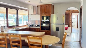 A modern kitchen with wooden cabinets, a central island with seating, and a view of the outdoors. - 5 BR House - Private Home on Shared Block (Frankston)
