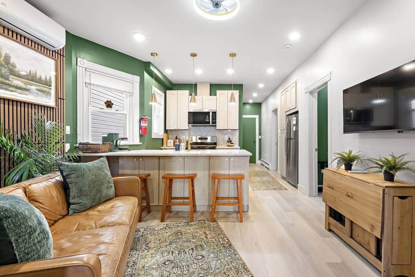 A modern kitchen with a central island, bar stools, a wooden cabinet, and a TV mounted on the wall.