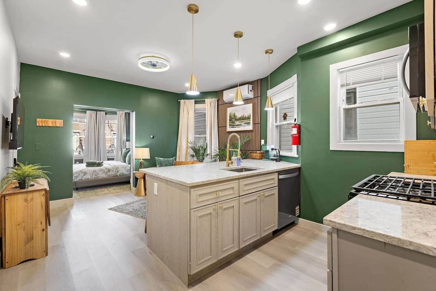 A modern kitchen with a central island, a dining area with a table and chairs, and a bedroom with a bed and curtains.