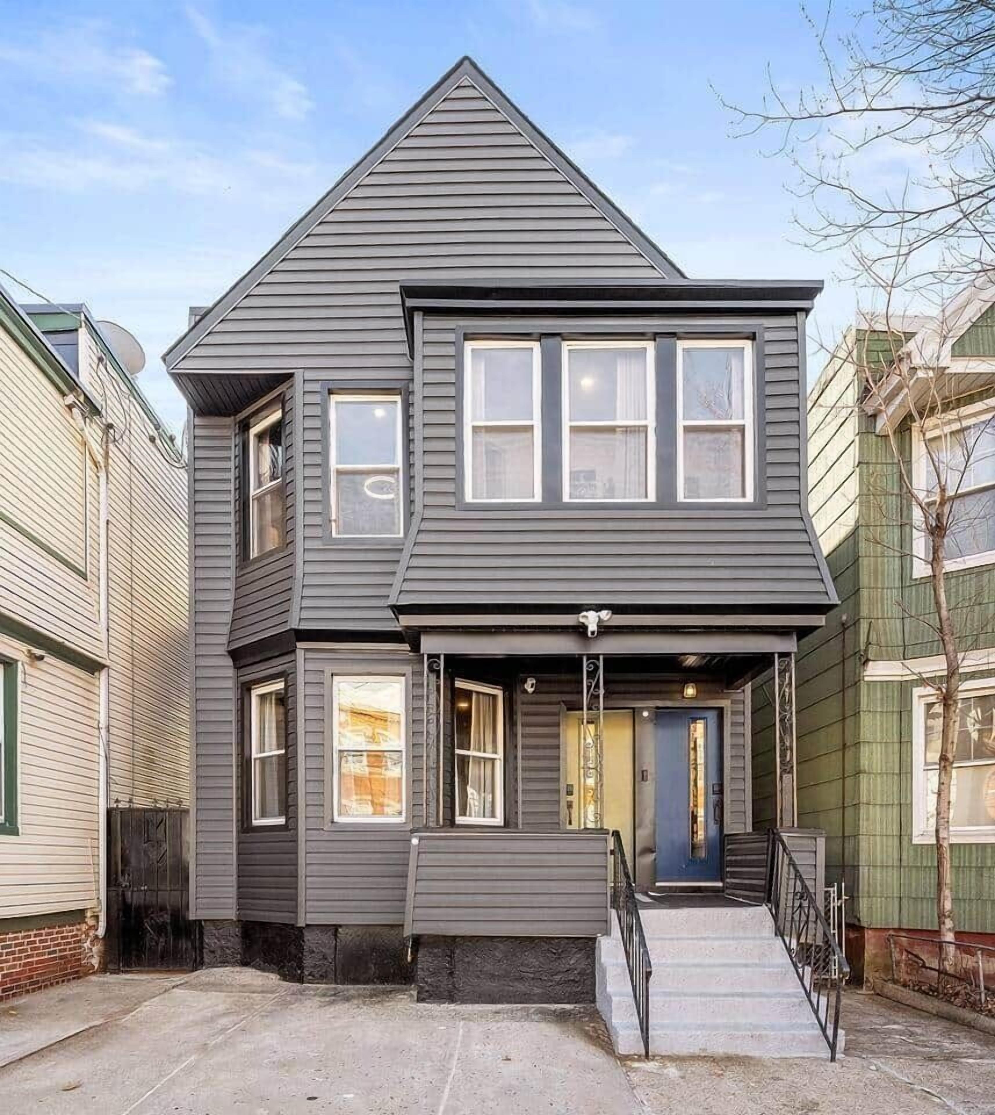 A two-story house with a gabled roof, a front porch with a black railing, and a blue door.