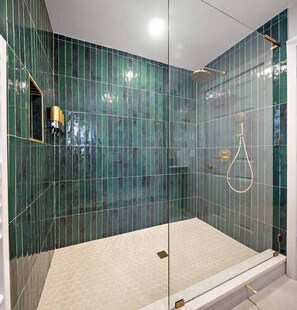 A glass-enclosed shower with a hexagonal floor tile design and a handheld showerhead. - Modern Verde • Chic 3BR • Easy NYC Commute (Jersey City)