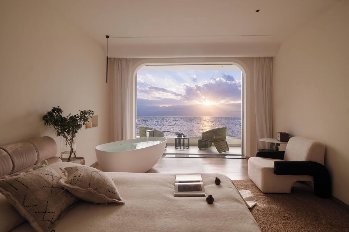 Un dormitorio moderno con una bañera grande, una cama, un sofá y vistas al mar.