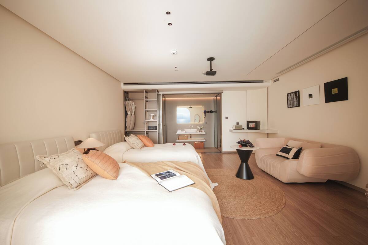 Una habitación de hotel moderna con una cama grande, un sofá, una mesita y un baño visible a través de una puerta abierta.