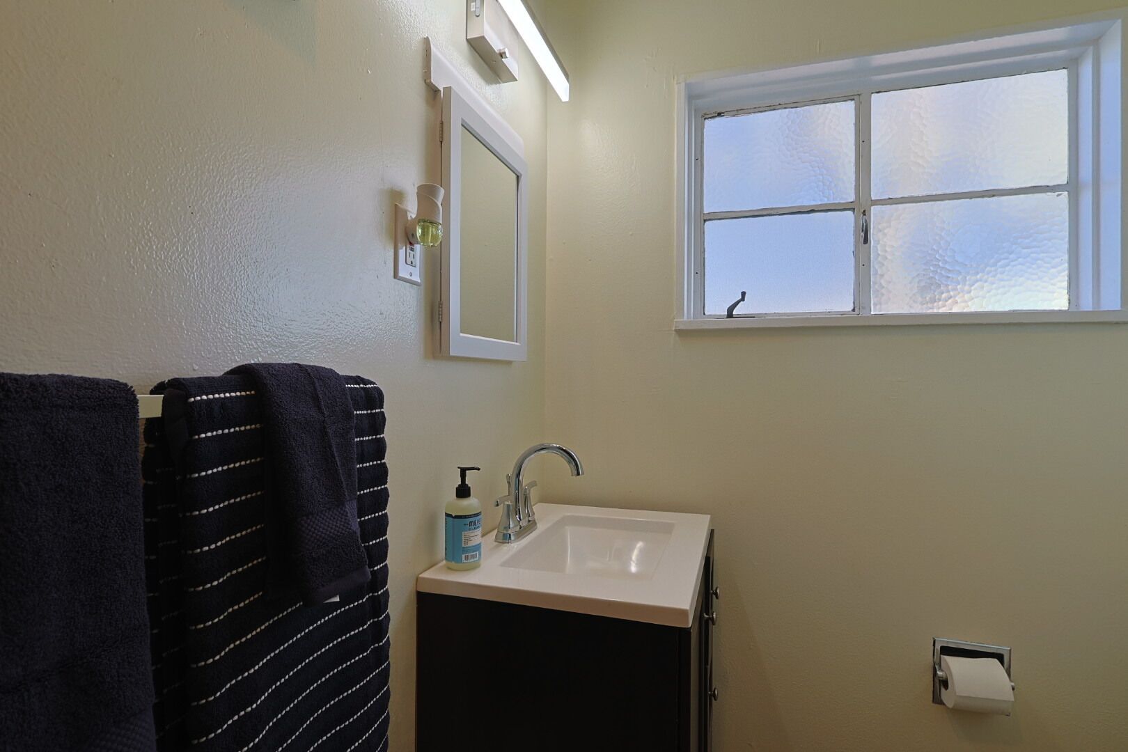 A bathroom with a sink, a mirror, a window, and a towel rack.