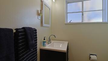 A bathroom with a sink, a mirror, a window, and a towel rack.