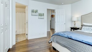 A bedroom with a bed, a nightstand, a lamp, and a door leading to another room. - Meridian Gem / 1 King+ 2 Queens / Central location (Meridian)