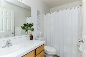 A bathroom with a white sink, mirror, toilet, and shower curtain. - Meridian Gem / 1 King+ 2 Queens / Central location (Meridian)