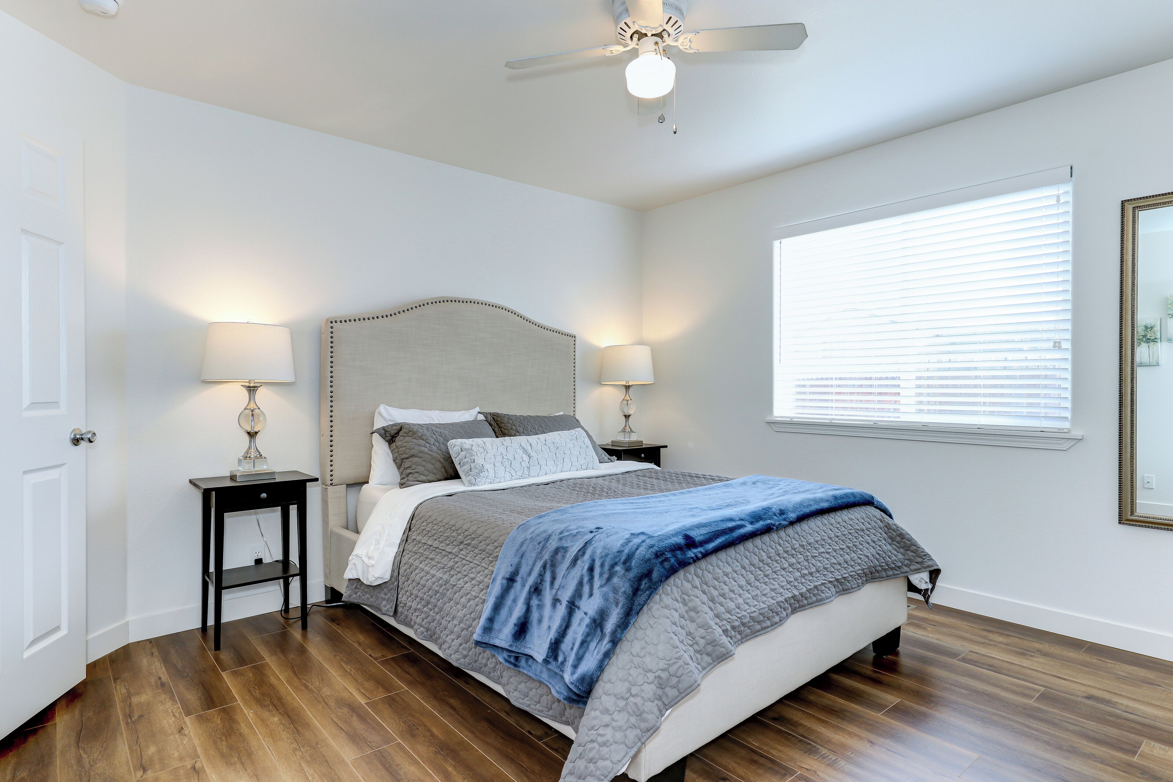 A bedroom with a bed, two bedside tables, a ceiling fan, and a window with blinds.
