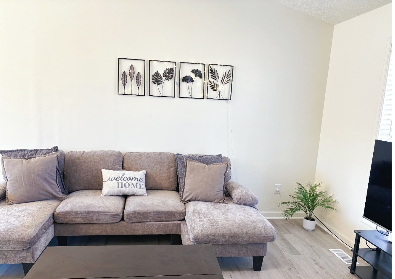 A living room with a beige sectional sofa, a coffee table, a flat-screen TV, and a wall-mounted plant.
