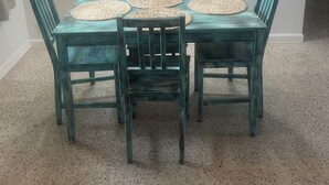 A dining area with a table set for four, surrounded by teal chairs, and a painting of a woman on the wall. - 2 bedroom unit 2 blocks to the beautiful gulf beaches (Treasure Island)