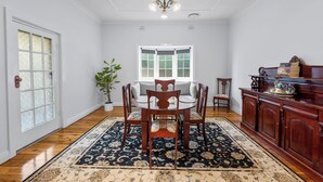 Een eetruimte met een ronde tafel, stoelen, een kroonluchter, een bloempot en een houten kast.
