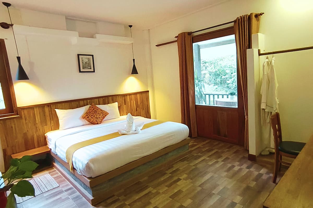 A neatly made bed with a wooden headboard, a bedside table, a hanging light, and a window with curtains.