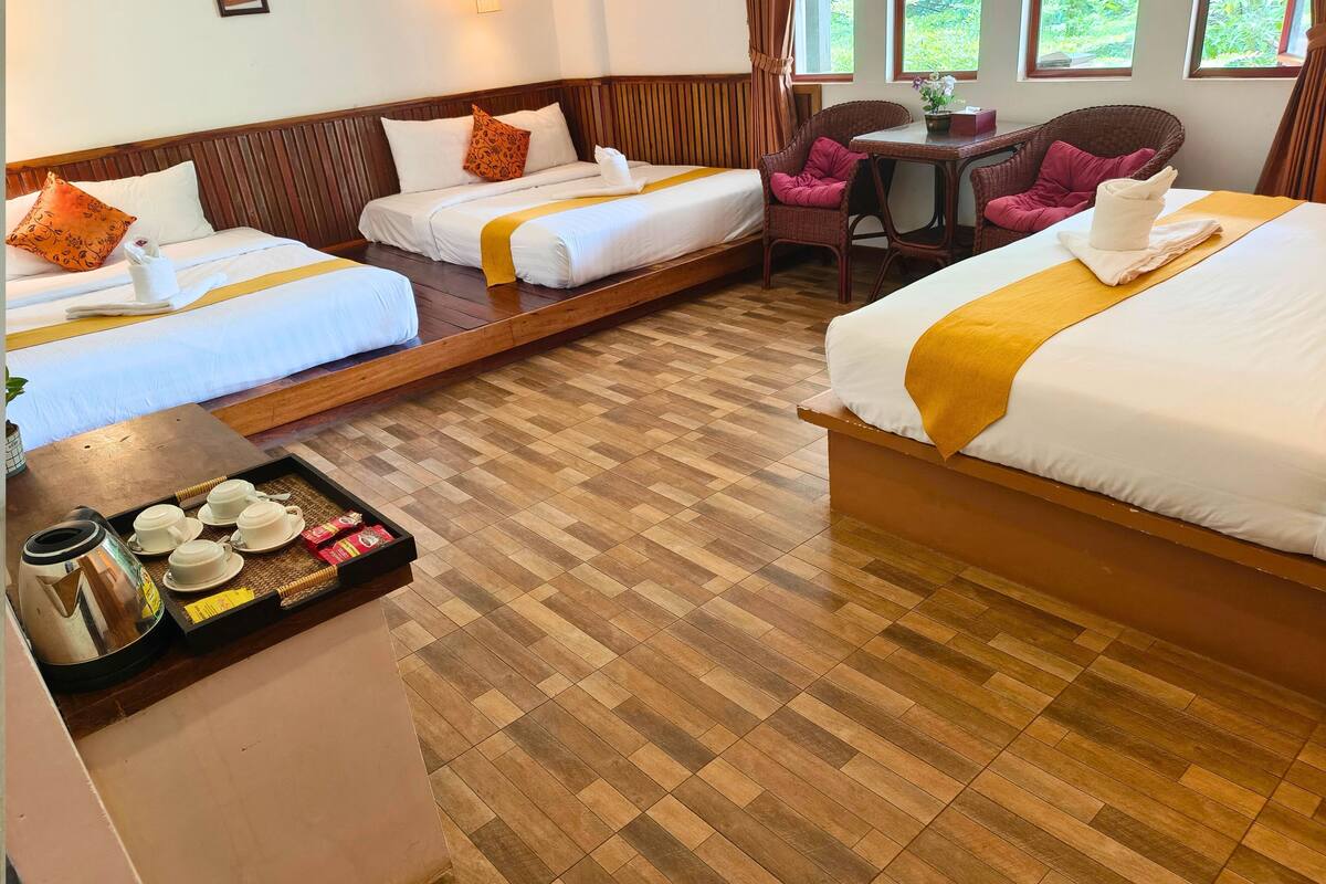 A hotel room with two beds, a wooden floor, a small table with a tray of tea and snacks, and wicker chairs.