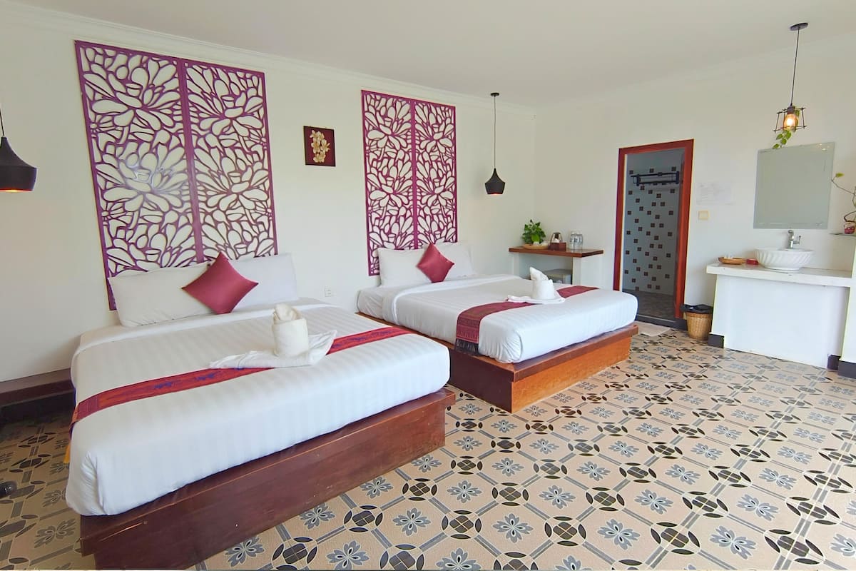 A hotel room with two beds, a small desk, a mirror, and a decorative wall panel.