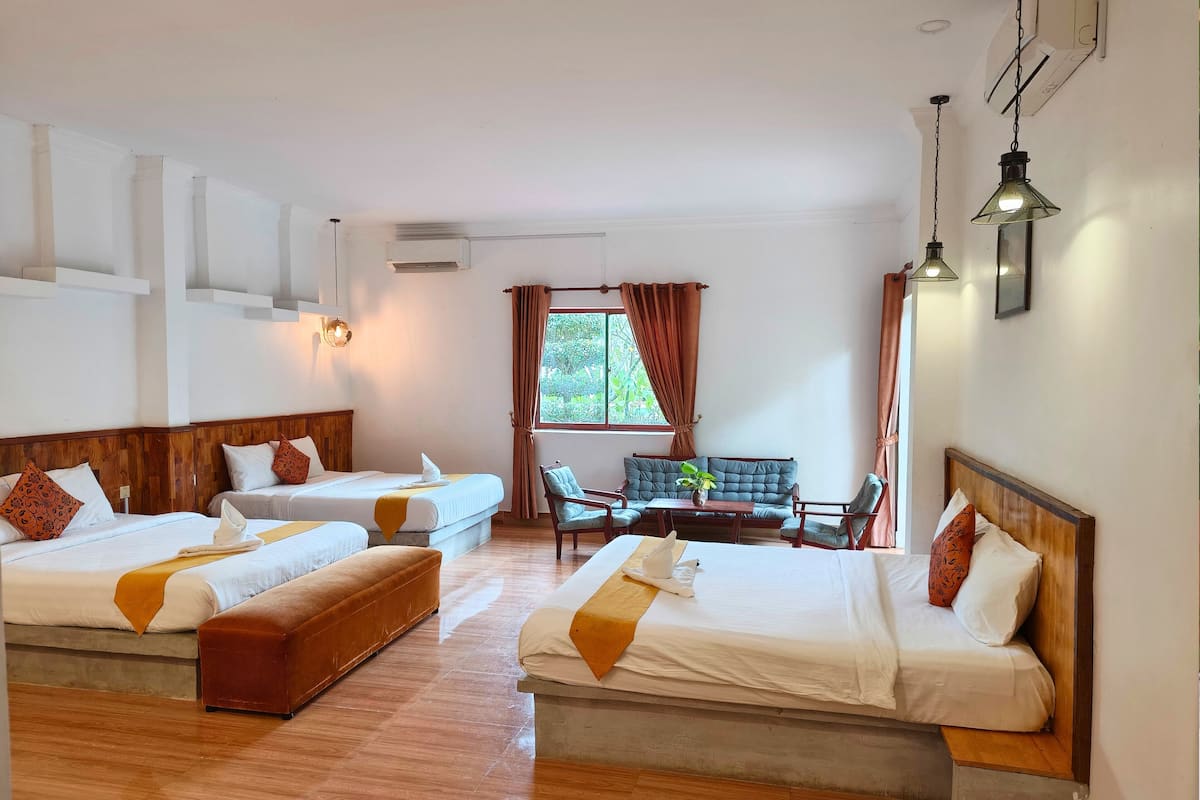 A hotel room with two single beds, a sofa, a small table, and a window with curtains.