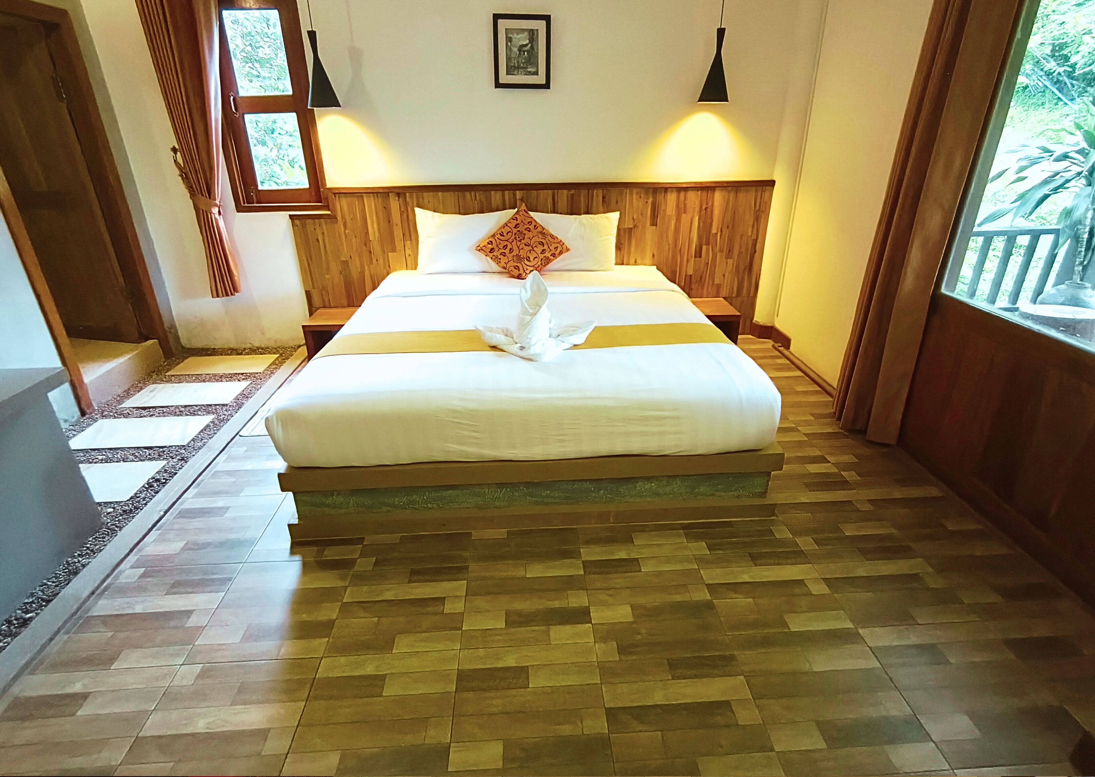 Un letto ben rifatto con una testiera in legno, un piccolo comodino e una finestra con tende.