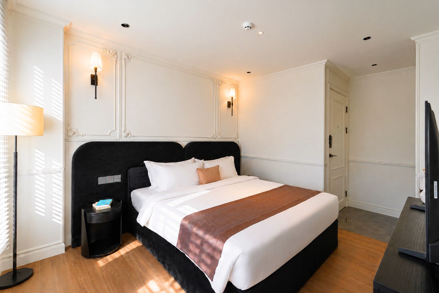 Una habitación de hotel con una cama grande, mesitas de noche, una lámpara y un televisor.