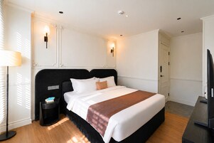 Una habitación de hotel con una cama grande, mesitas de noche, una lámpara y un televisor.
