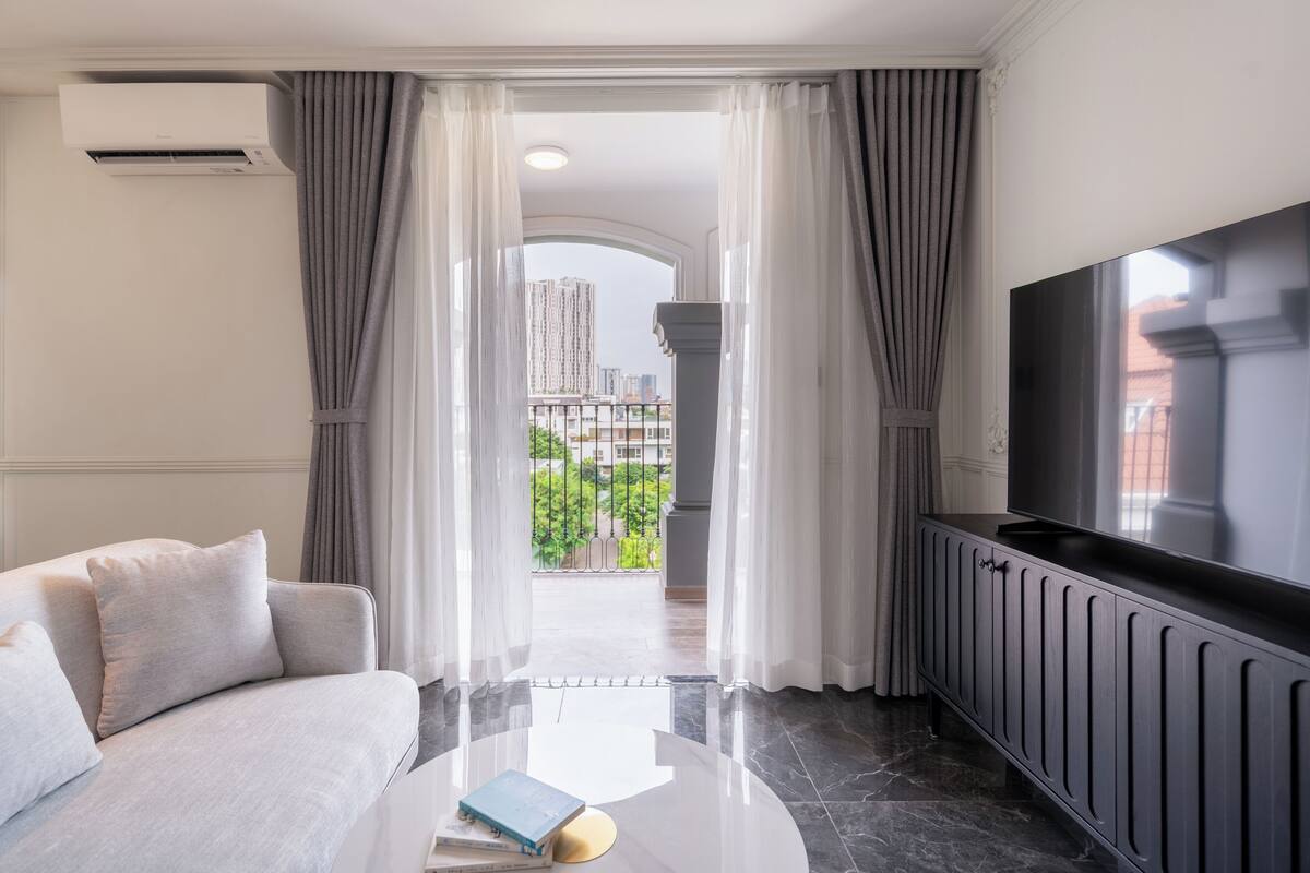 Un salon moderne avec un canapé, un téléviseur à écran plat et un balcon agrémenté de rideaux.