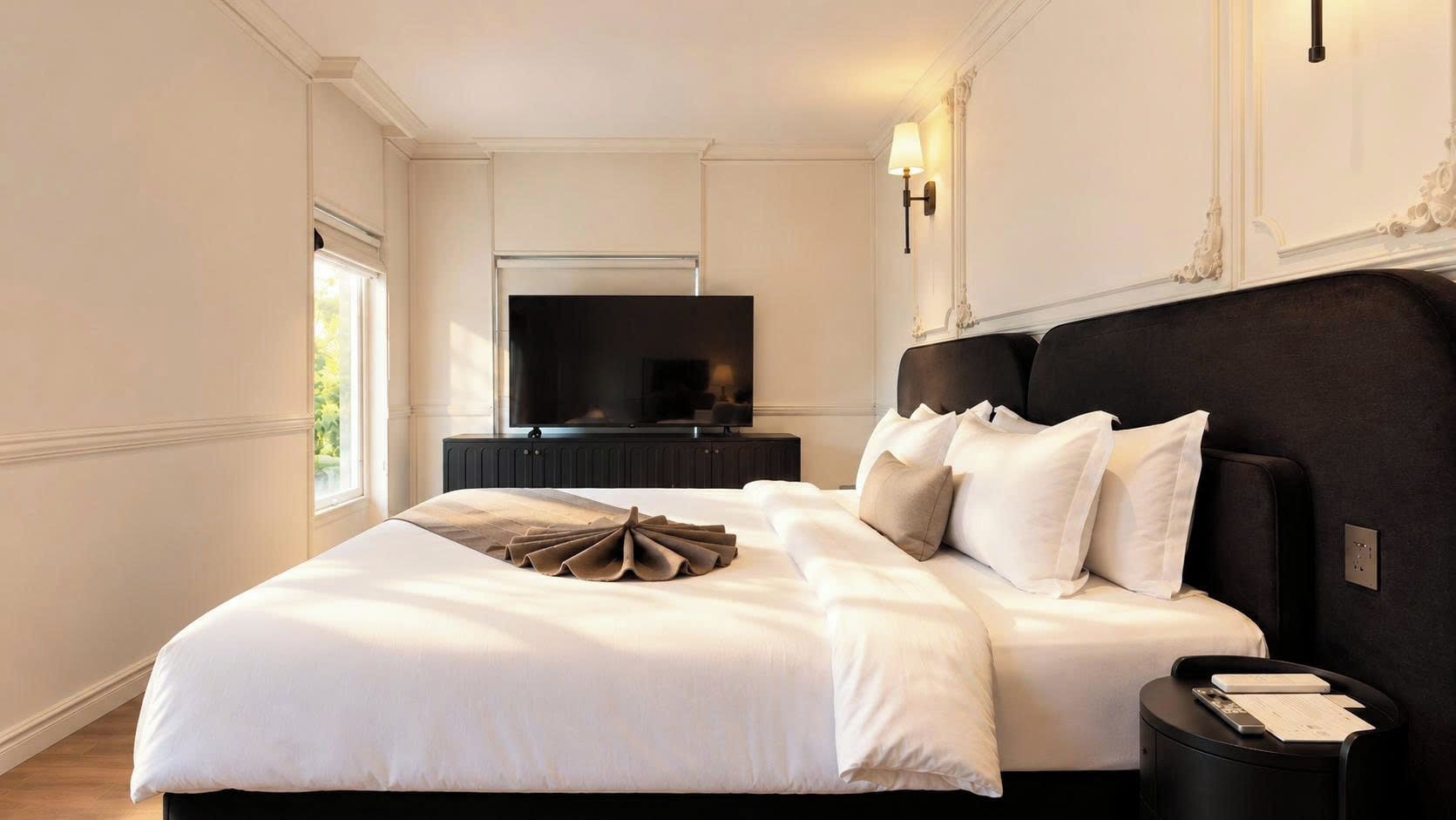 Una habitación de hotel con una cama grande, televisor, mesita de noche y lámpara de pared.