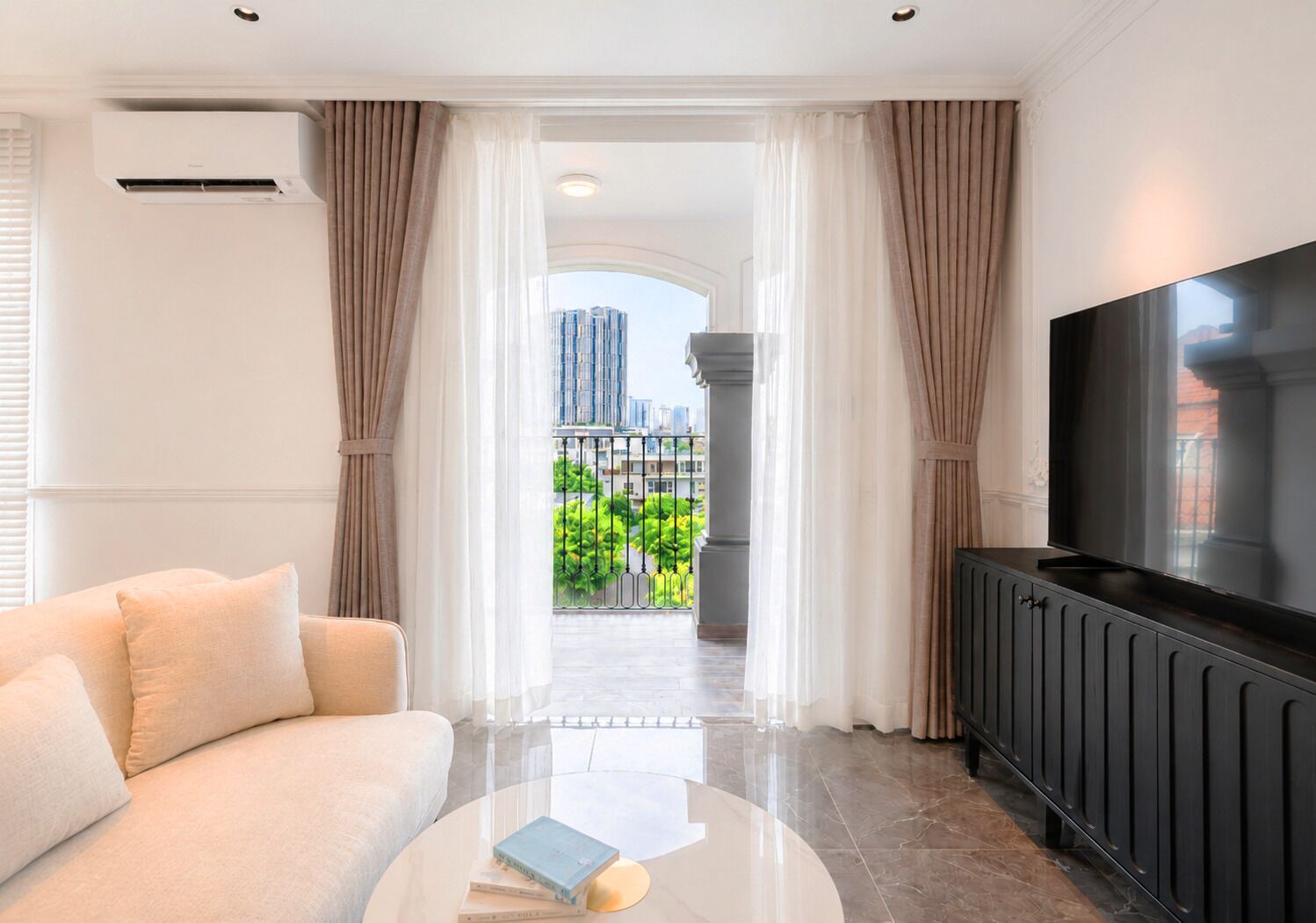 A modern living room with a sofa, a coffee table with books, a flat-screen TV, and a view of a cityscape through a large window.