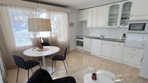 A modern kitchen with white cabinets, a microwave, and a dishwasher. There is a dining area with a round table and two chairs. - Haus Rupicapra by Interhome (Arosa)