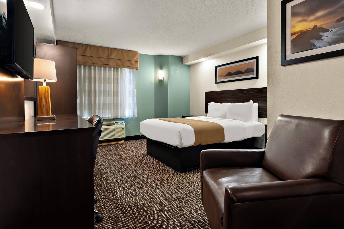 A hotel room with a bed, a desk, a chair, and a television.