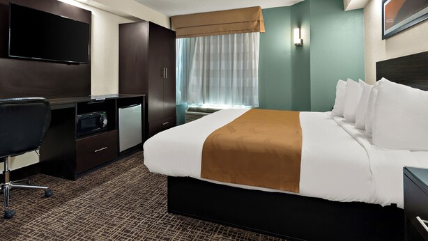 A hotel room with a large bed, a desk with a flat-screen TV, a microwave, and a small refrigerator. - The Point Hotel (Memphis)