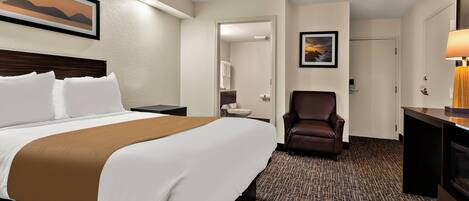 A hotel room with a bed, a desk, a chair, a bathroom, and a painting on the wall.
