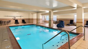 An indoor swimming pool with clear lane markings, a lifeguard chair, and a seating area with chairs and tables. - The Point Hotel (Memphis)