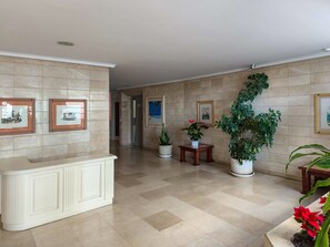 A lobby with a tiled floor, a reception desk, framed artwork, and potted plants. - Mirador del Puerto by Lica Homes (Estepona)