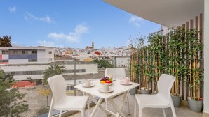 Ein Balkon mit Tisch für zwei Personen, weißen Stühlen und einer Wand mit Topfpflanzen.