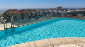 Ein Pool auf dem Dach mit klarem, blauem Wasser, umgeben von Gebäuden und Blick auf das Meer.