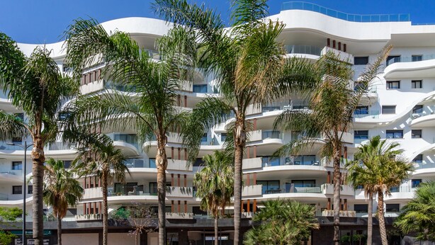 Ein mehrstöckiges Hotel mit Balkonen, Palmen und blauem Himmel.