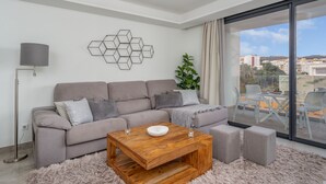 Ein modernes Wohnzimmer mit einem grauen Sofa, einem Holztisch und einem großen Fenster mit Blick auf die Stadt.