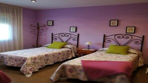 Habitación con dos camas, cada una con ropa de cama floral y almohadas verdes, paredes moradas y suelo de madera.