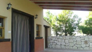 Un espacio exterior cubierto con pared de piedra, piso de baldosas y una puerta grande con cortinas.