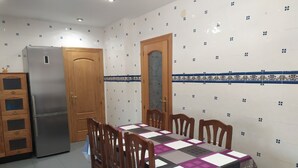 Una cocina con una mesa de comedor, sillas, un refrigerador, armarios de madera y azulejos con diseño.