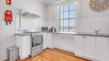 A modern kitchen with white cabinetry, a stainless steel stove, a microwave, and a large window.